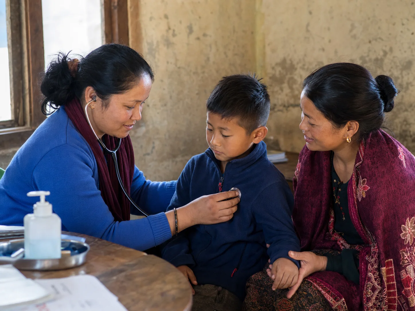 A community health worker caring for a young boy while his mother sits beside him